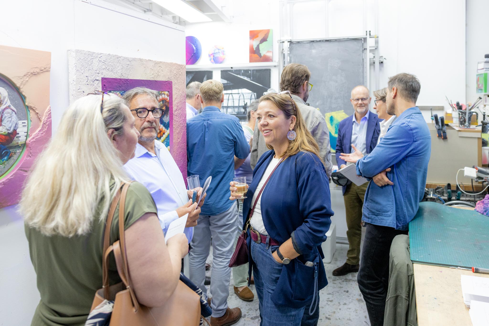 Petit groupe de participants en conversation animée devant des œuvres aux tons magenta, dans un atelier