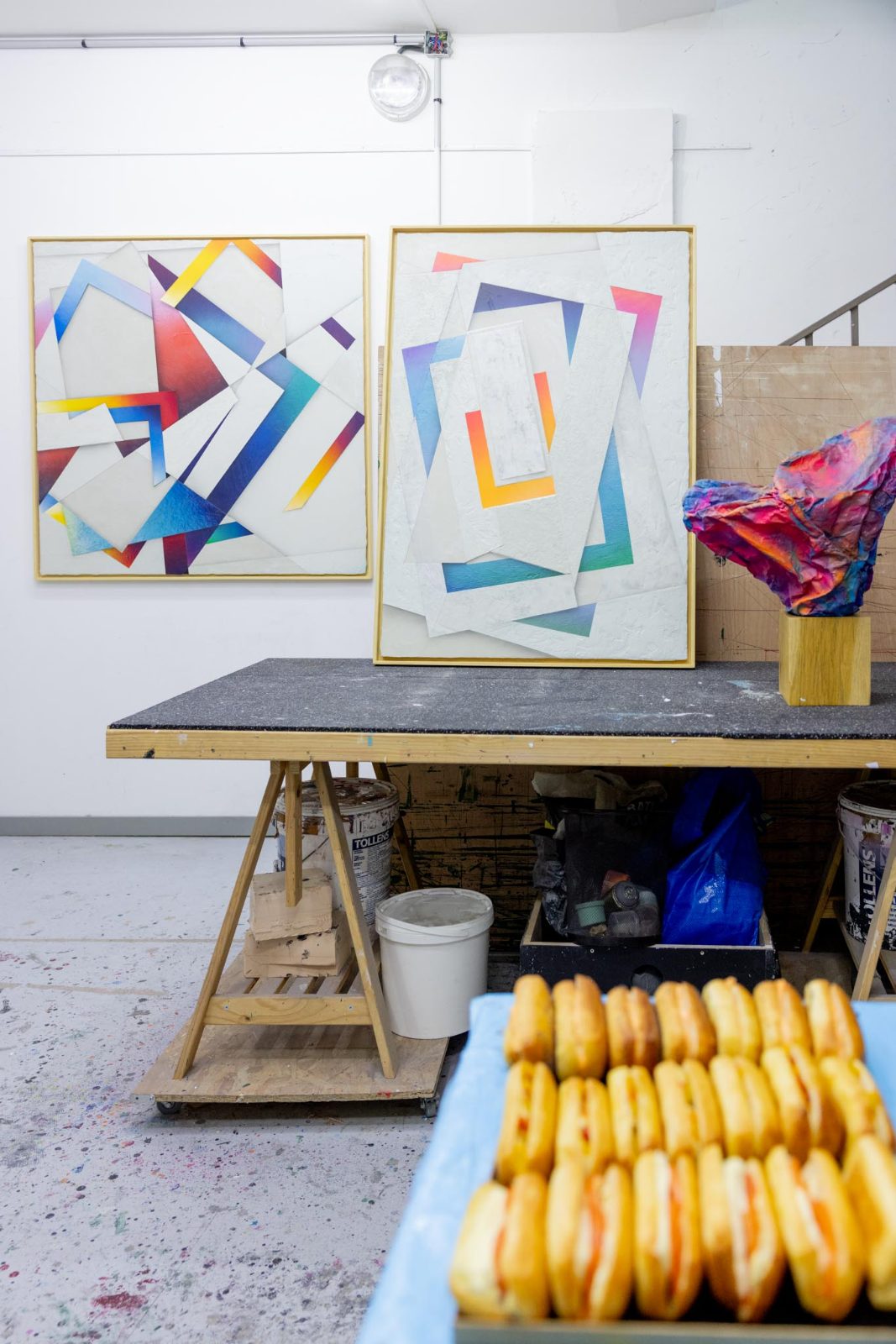 Deux grandes toiles géométriques encadrées posées dans un atelier, à côté d'une table dressée pour le buffet