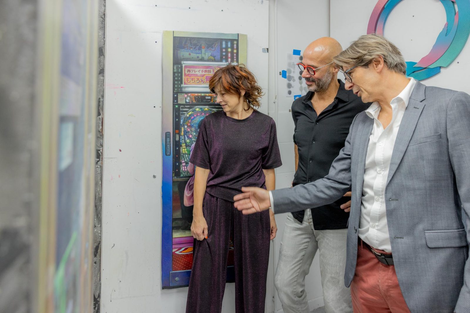 Trois participants observent ensemble une grande peinture, l'un d'eux la désigne de la main